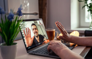 A retired woman communicates with her son via video link, uses a laptop for communication at home.